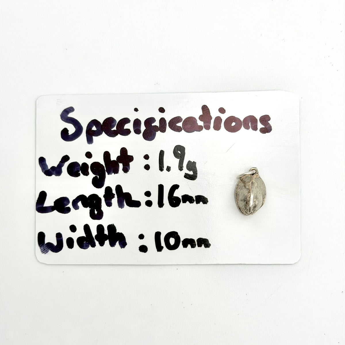 A small metallic pendant or charm displayed next to a white card labeled 'Specifications' with handwritten measurements and weight details.