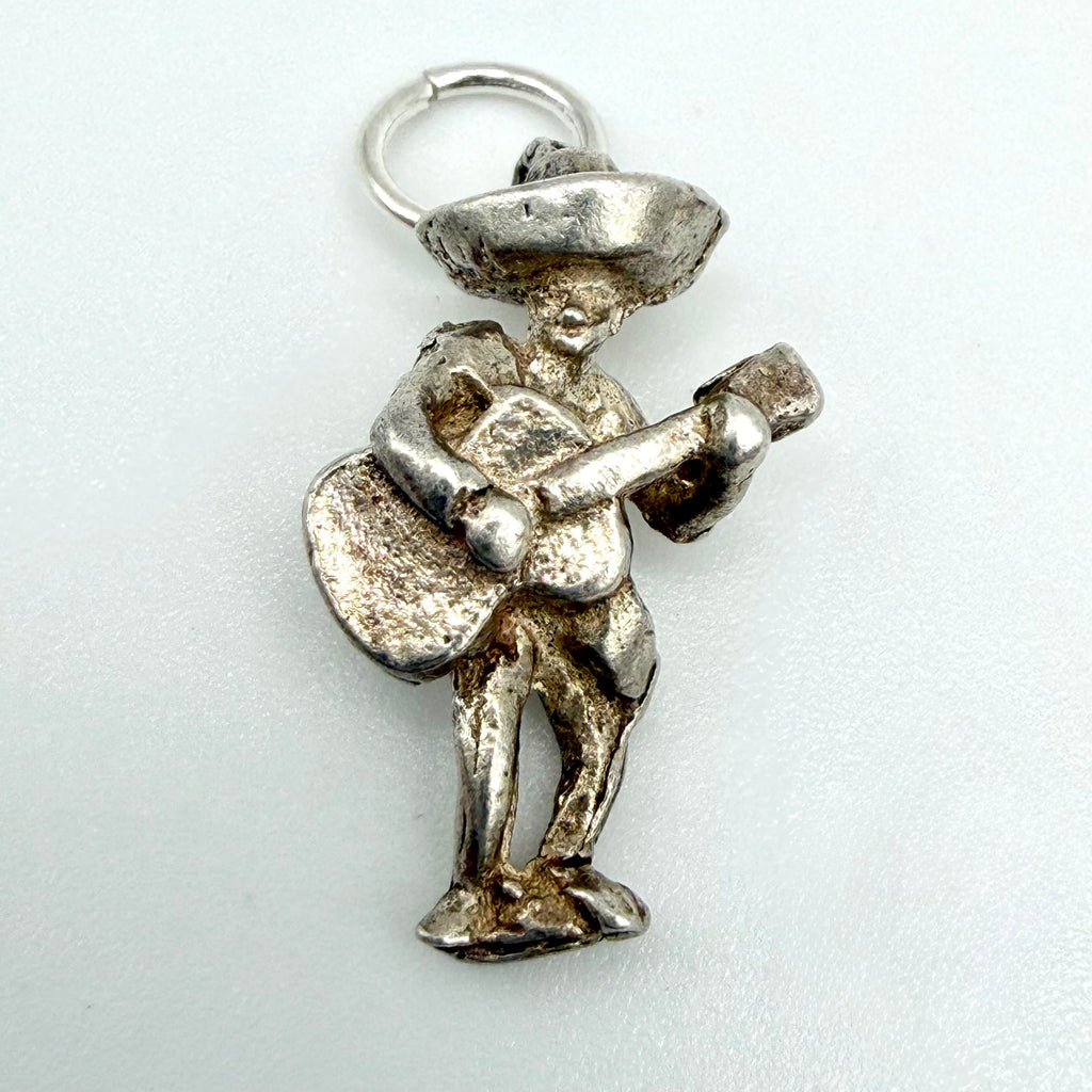 A silver Mexican musician charm pendant featuring a detailed figure playing a guitar and holding a sombrero, shown on a plain light background.