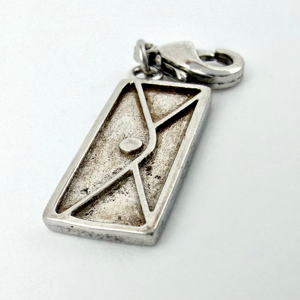 A rectangular silver pendant with an embossed envelope design and a lobster clasp, shown on a plain light background.