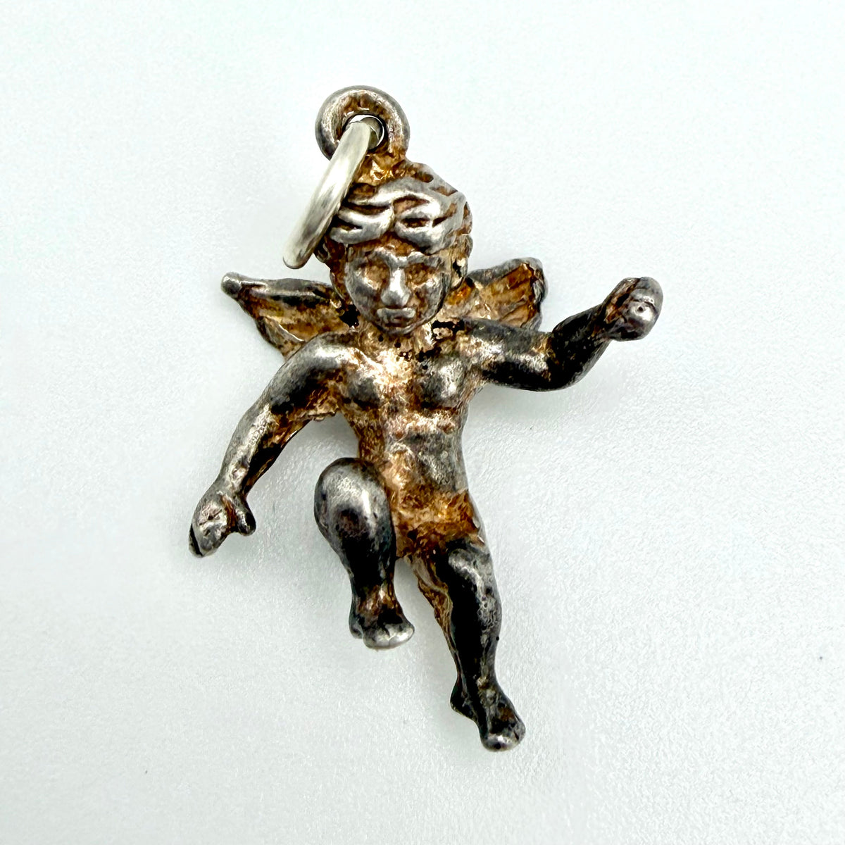 A small cherub or cupid pendant charm in oxidized silver-tone metal with warm gold-toned highlights, shown on a plain light background.