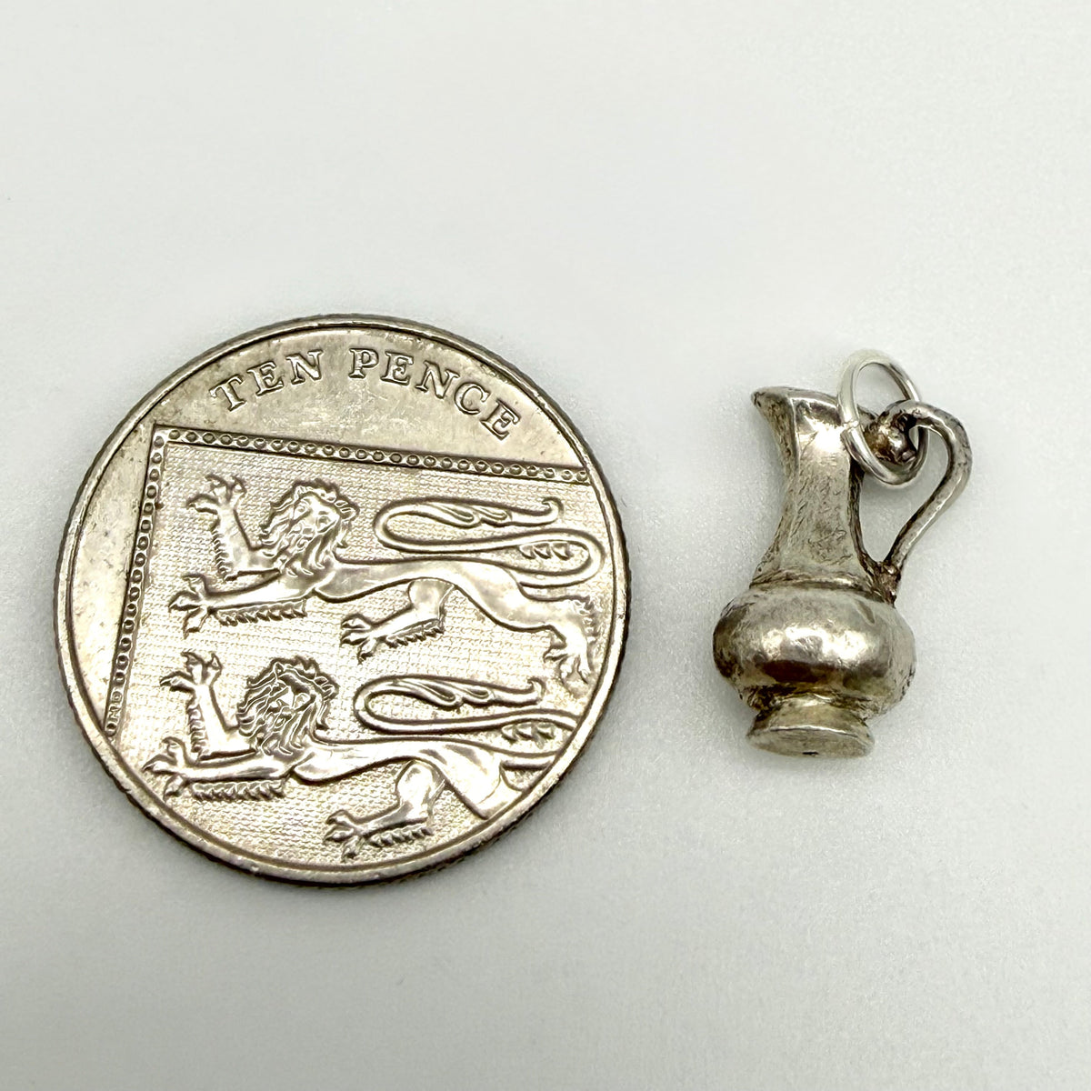 Sterling silver Aquarius water jug charm beside a ten pence coin for scale