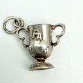 A silver trophy cup pendant charm with two handles, a small loop at the top, and the letters 'FA' engraved on the front, shown on a plain light background.