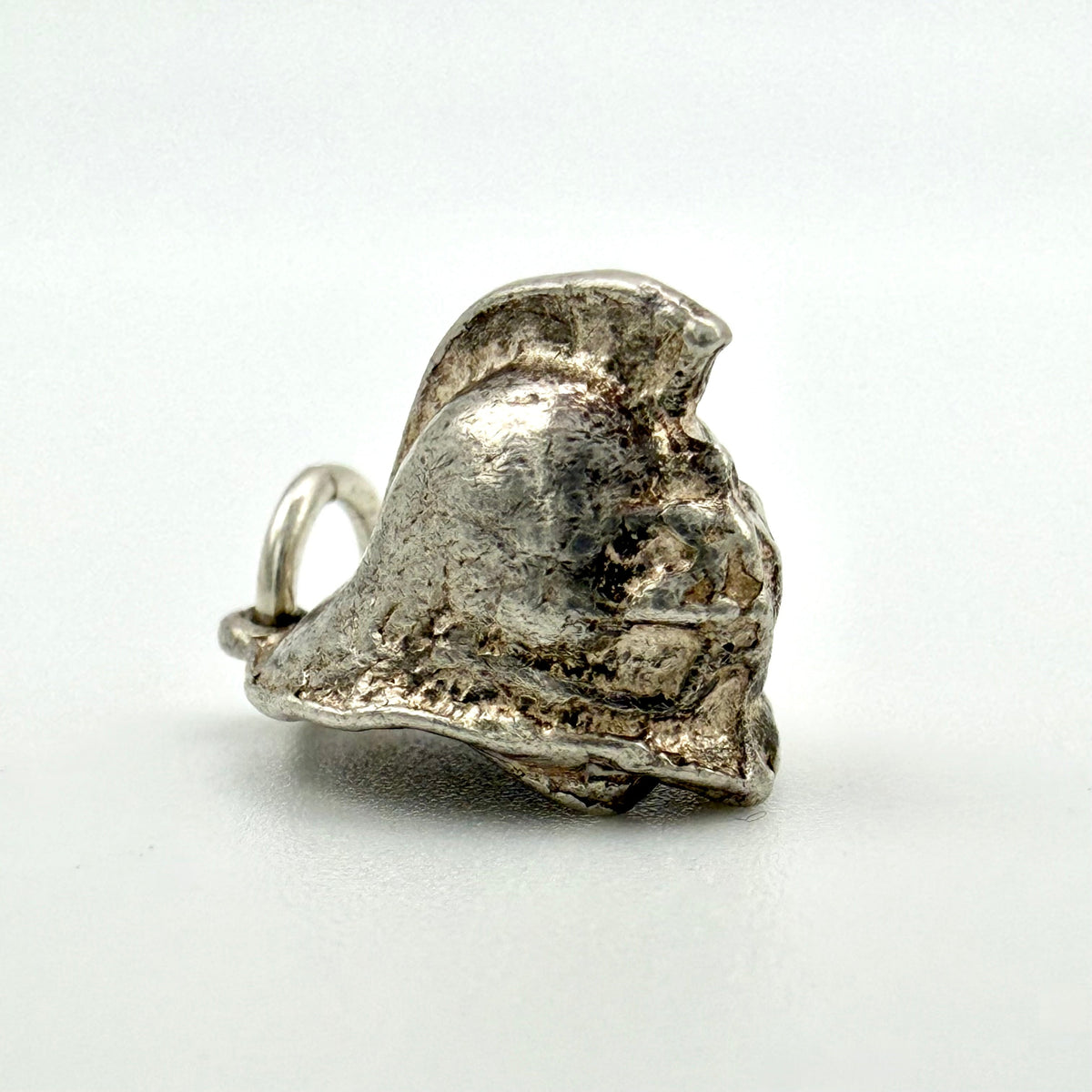 A small Silver charm shaped like a stylized Fireman’s Helmet with a loop at the top, photographed on a plain light background.