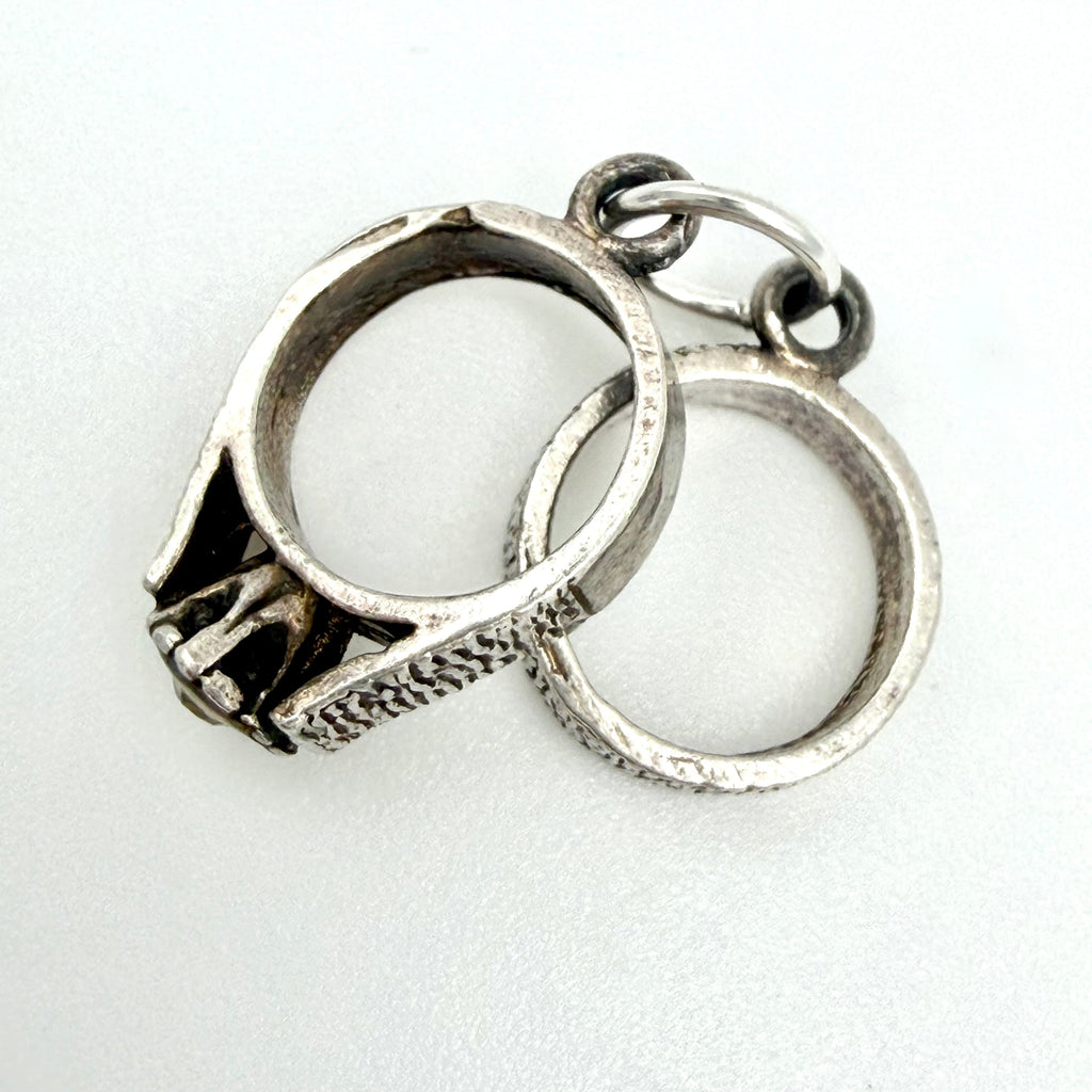 Front view of vintage sterling silver linked rings charm with textured bands and a small clear stone