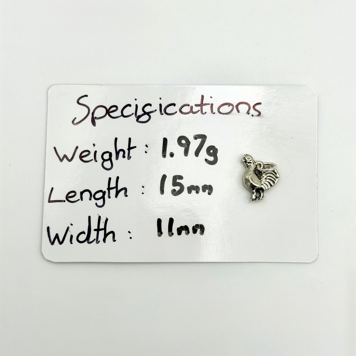 Cockerel charm beside a card showing its 1.97g weight and 15mm by 11mm size
