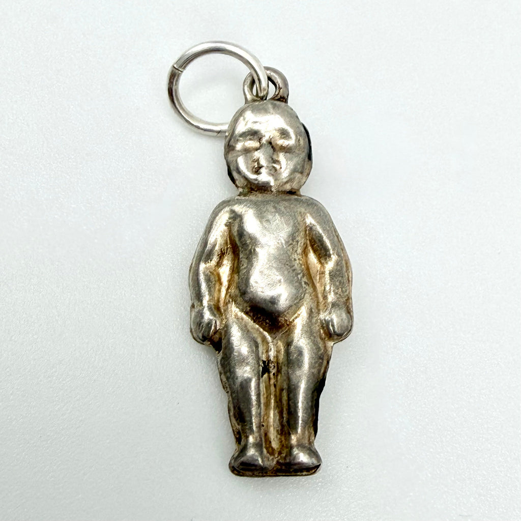 A small metallic figurine charm shaped like a standing nude child, attached to a silver ring, photographed against a plain light background.