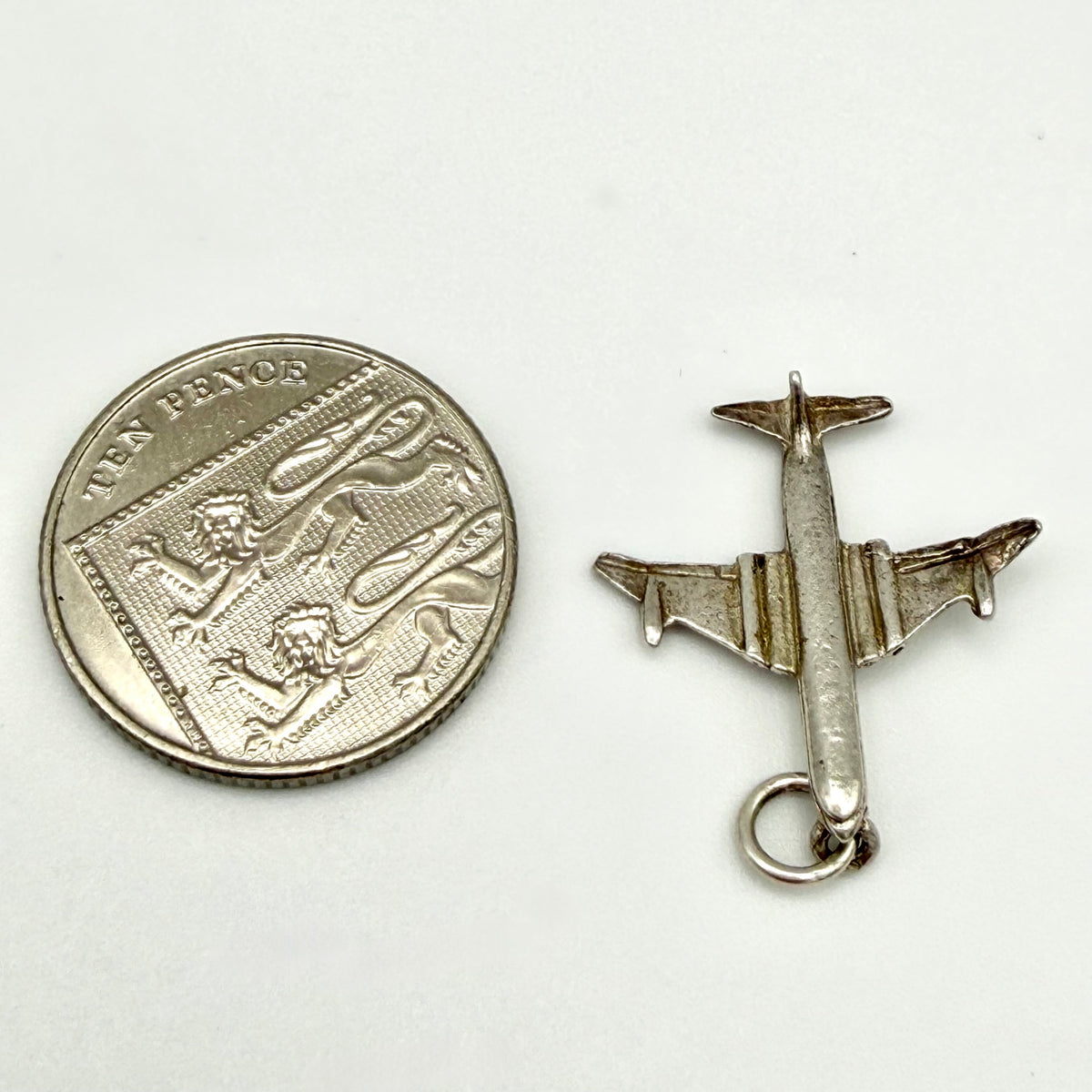 A small silver airplane charm or pendant shown next to a coin for scale on a plain white background.