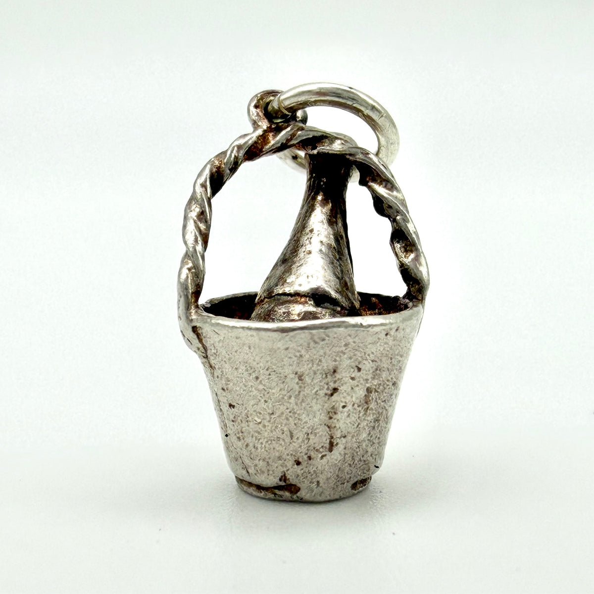 A sterling silver charm shaped like a small bucket with a twisted handle and a conical top detail, shown on a plain white background.
