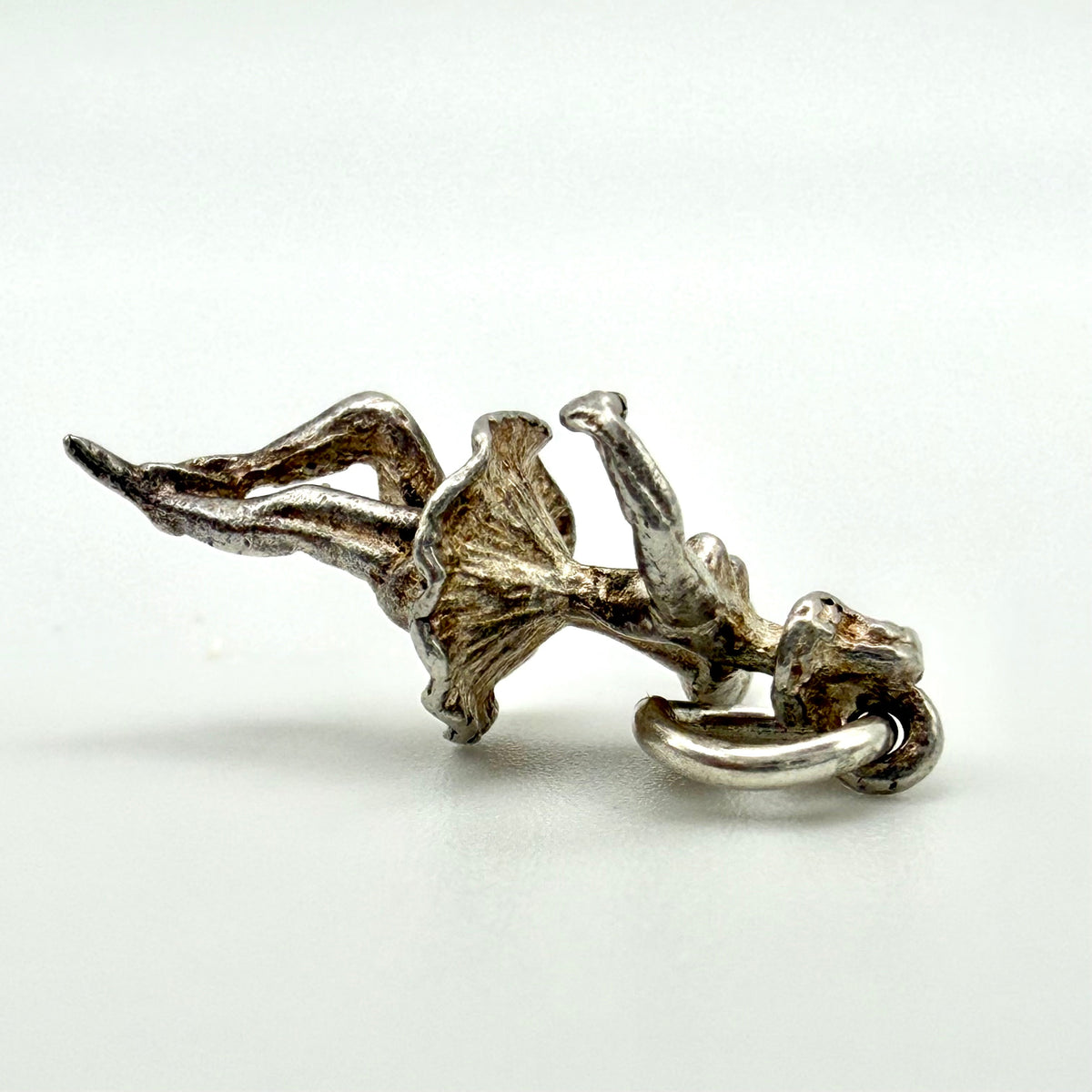 A silver charm shaped like a stylized, dynamic human figure in a flared dress, photographed on a plain light background.