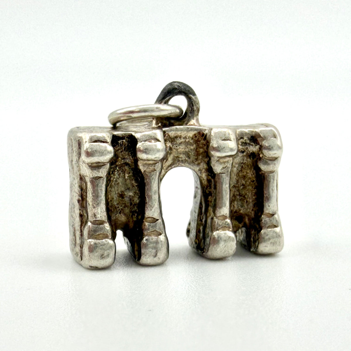 A silver-toned metal pendant shaped like a three-bone arch, photographed on a plain white background.