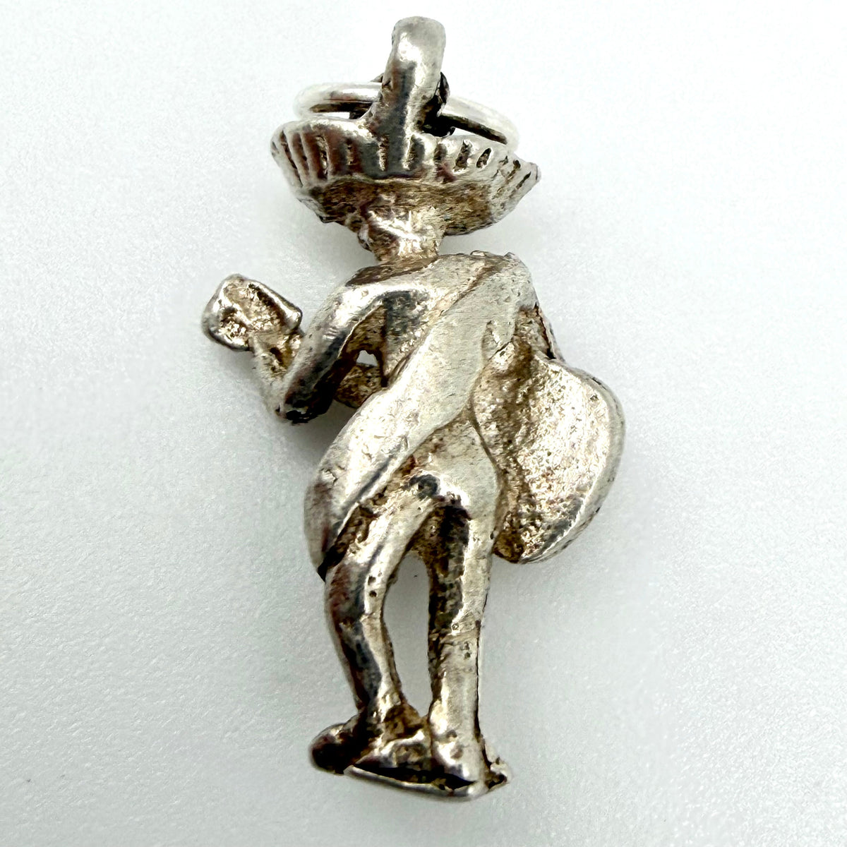 A sterling silver pendant shaped like a stylized figure wearing a sombrero and holding a small object, photographed on a plain light background.