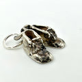 A pair of miniature silver baby boot charms with a distressed, oxidized finish and a small silver keyring attached, shown on a plain white background.