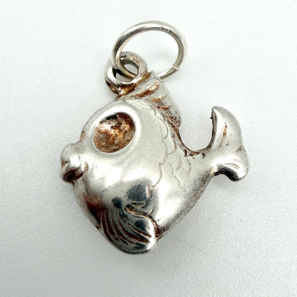Vintage sterling silver fish charm lying beside a ten pence coin to show its small size