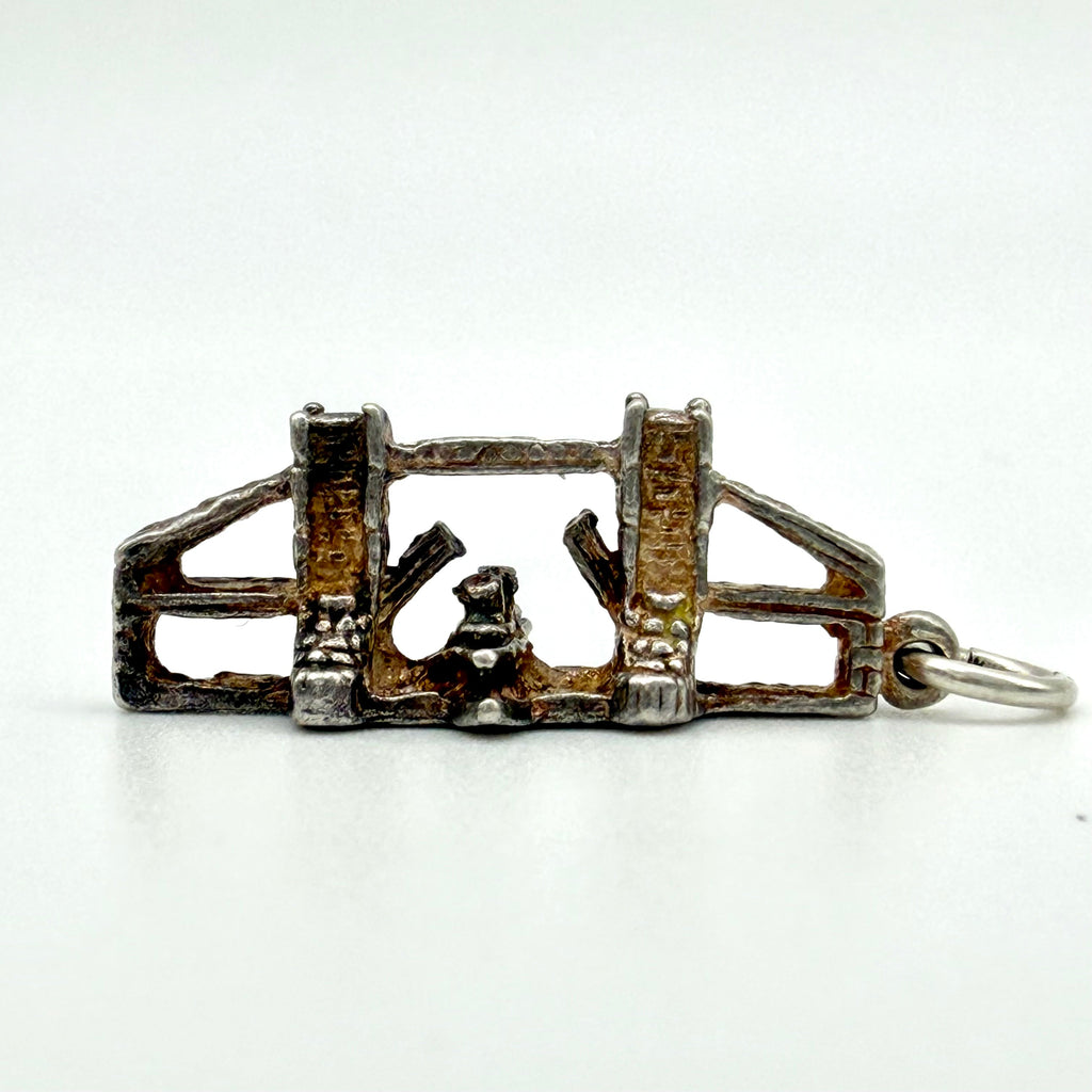 A small silver-toned metal charm or pendant with a rustic, oxidized brown finish, featuring a small central figure and a split ring attachment, shown on a plain white background.