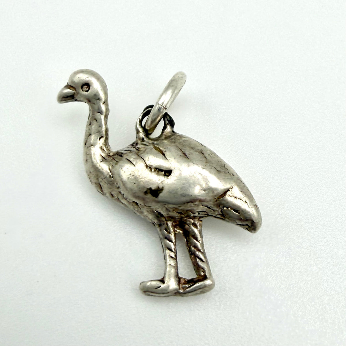 A silver-toned metal bird charm, shaped like a small ostrich or emu with a textured finish and a hanging loop at the top, shown on a plain light background.