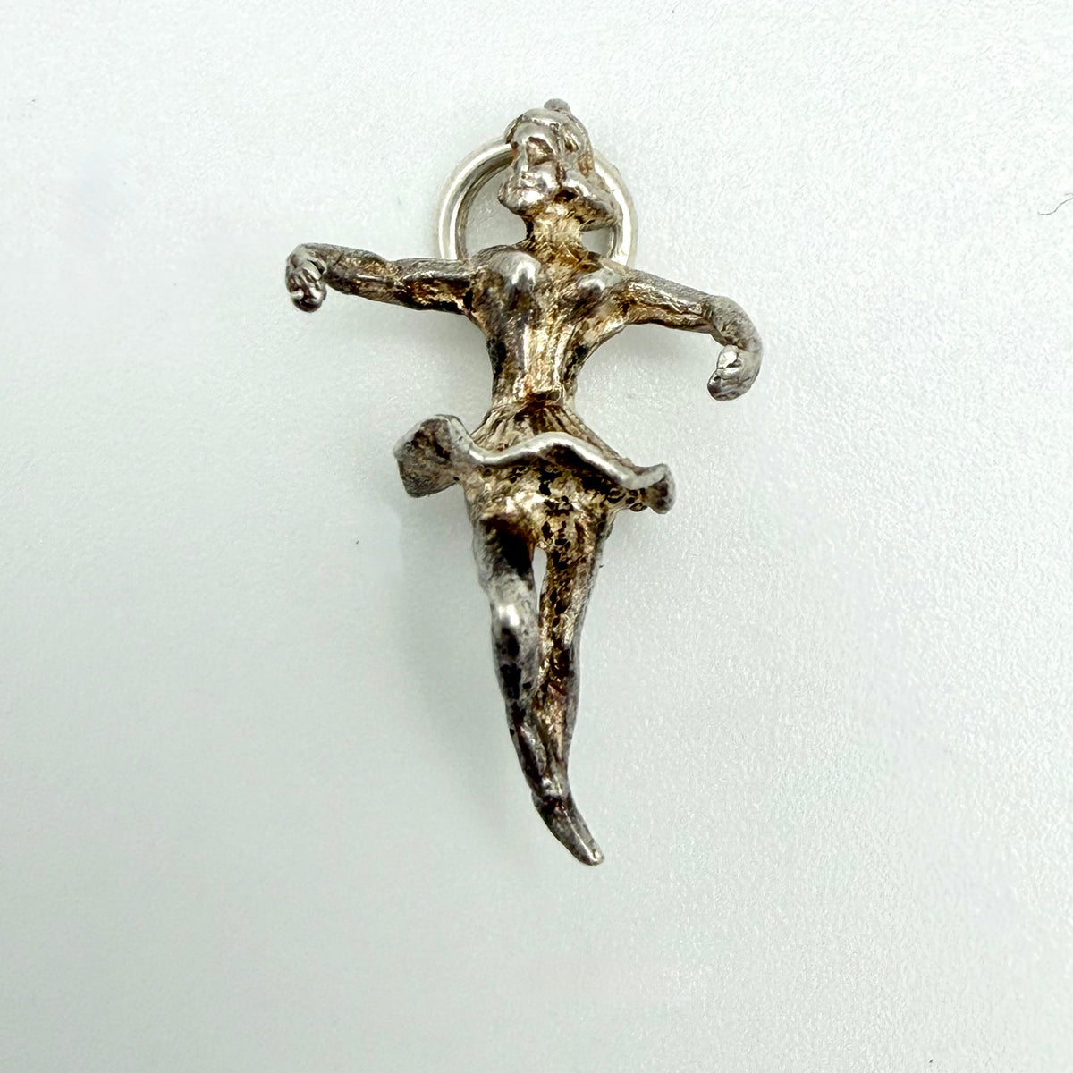 A small silver charm shaped like a dancing female figure with outstretched arms and a ring loop at the top, shown on a plain light background.