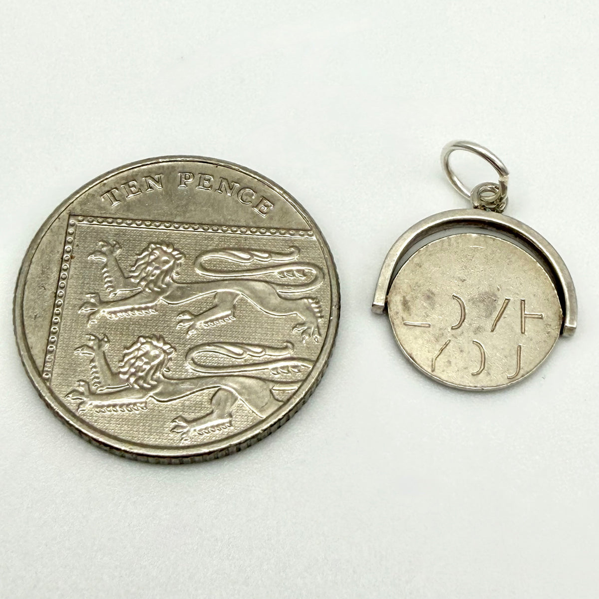 Sterling silver spinning fob charm shown beside a ten pence coin for scale