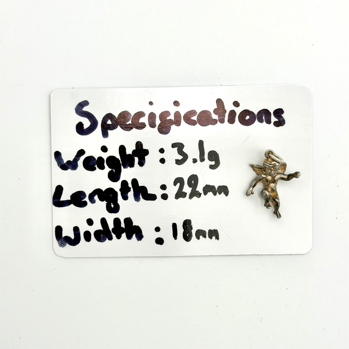 A small metallic figurine of a winged cherub or cupid is shown next to a white card with handwritten specifications listing its weight, length, and width.