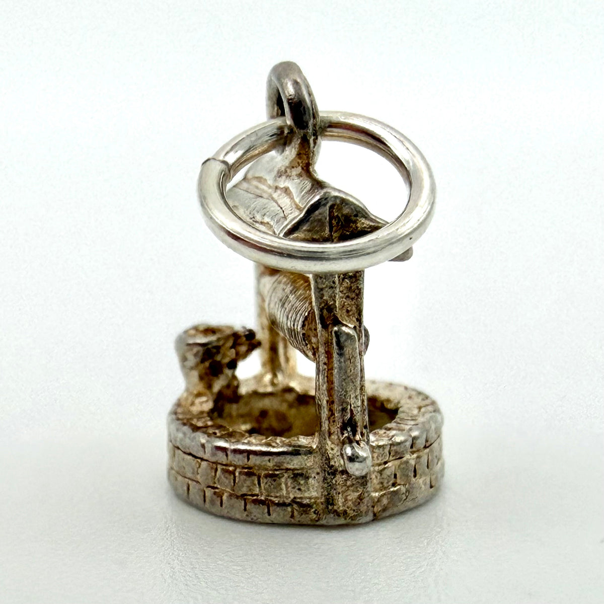 Front view of vintage silver wishing well charm showing winding handle and stonework