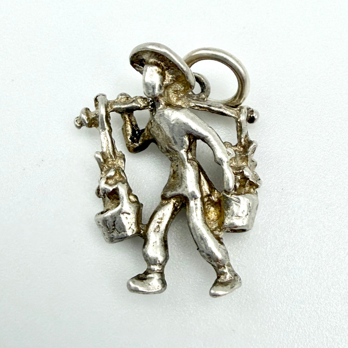 A sterling silver charm shaped like a farmer carrying baskets on his shoulders, shown on a plain white background.