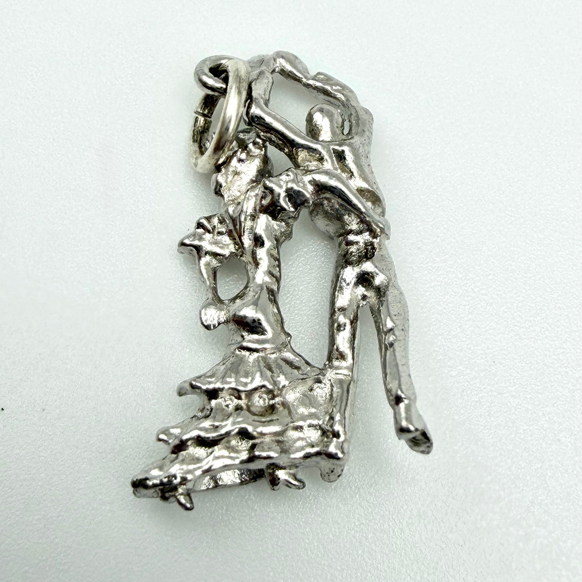 A sterling silver pendant featuring an abstract, textured depiction of two dancing figures, photographed on a plain light background.