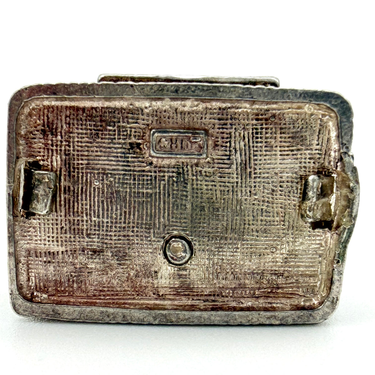 A vintage silver-toned metal case or compact, showing the textured back side with a stamped 'C.V.