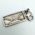 A silver metal charm shaped like an envelope with a textured, antiqued center and a lobster clasp attached on the right side, shown on a light gray background.