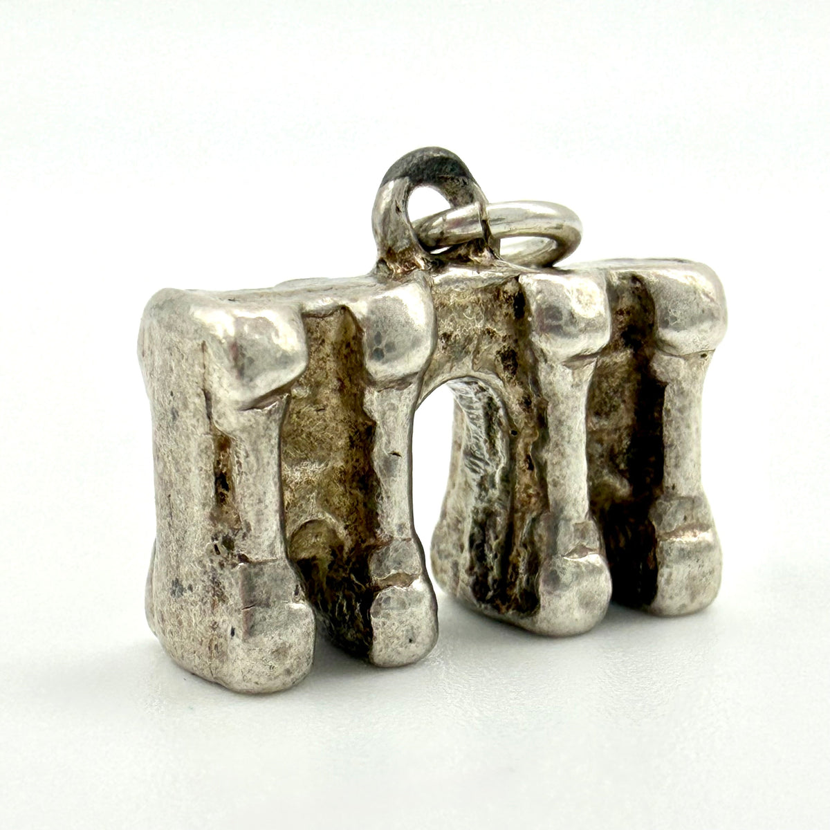 A textured sterling silver pendant shaped like a stylized arch bridge, featuring a polished bail at the top, photographed on a clean white background.