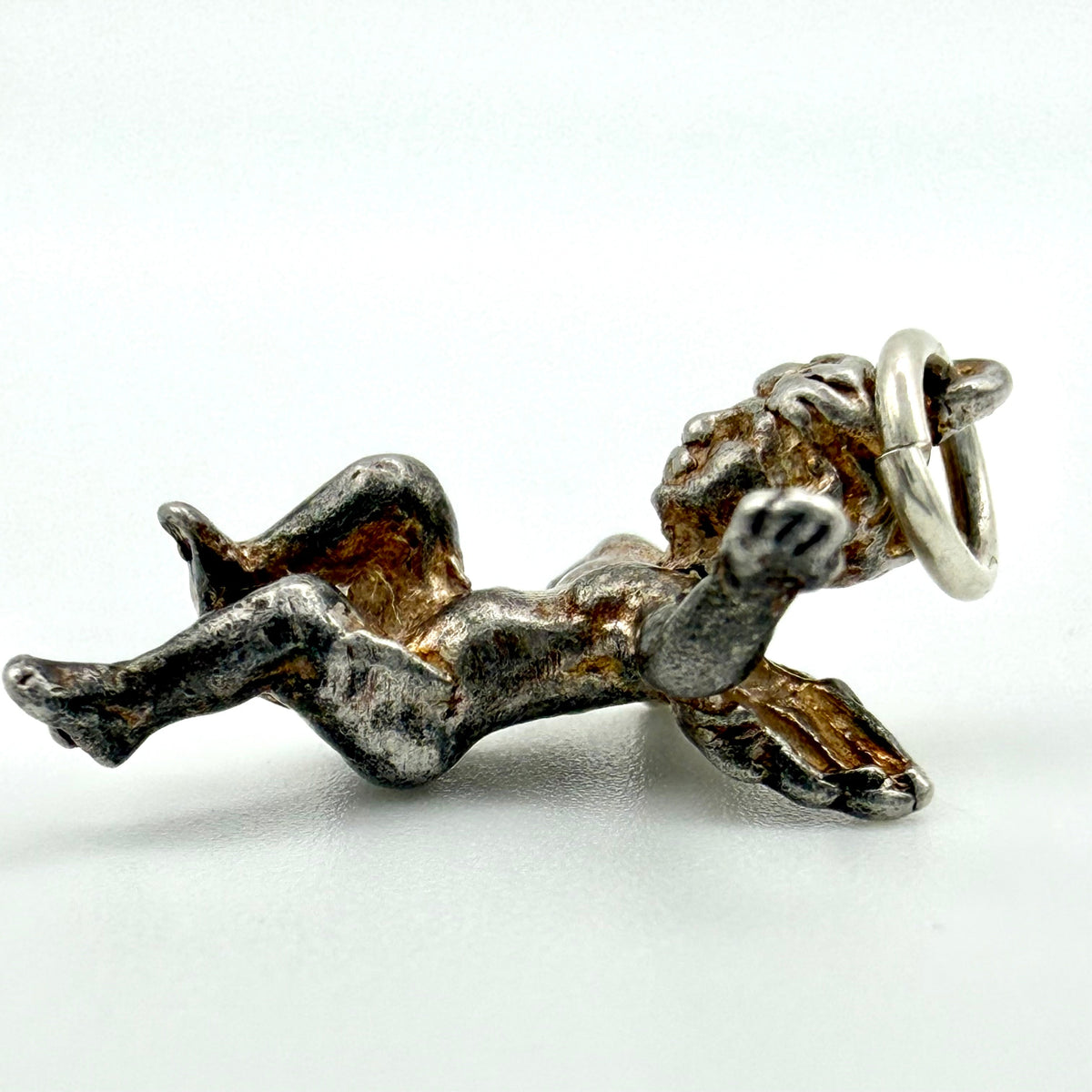 A small metallic cherub or angel charm lying on its side, holding a ring in its raised hand. The charm has a textured, oxidized silver finish with dark recessed areas, photographed on a plain light background.