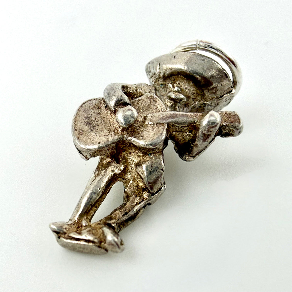 A small silver-toned metal charm shaped like a seated figure playing a guitar, photographed on a plain white background.