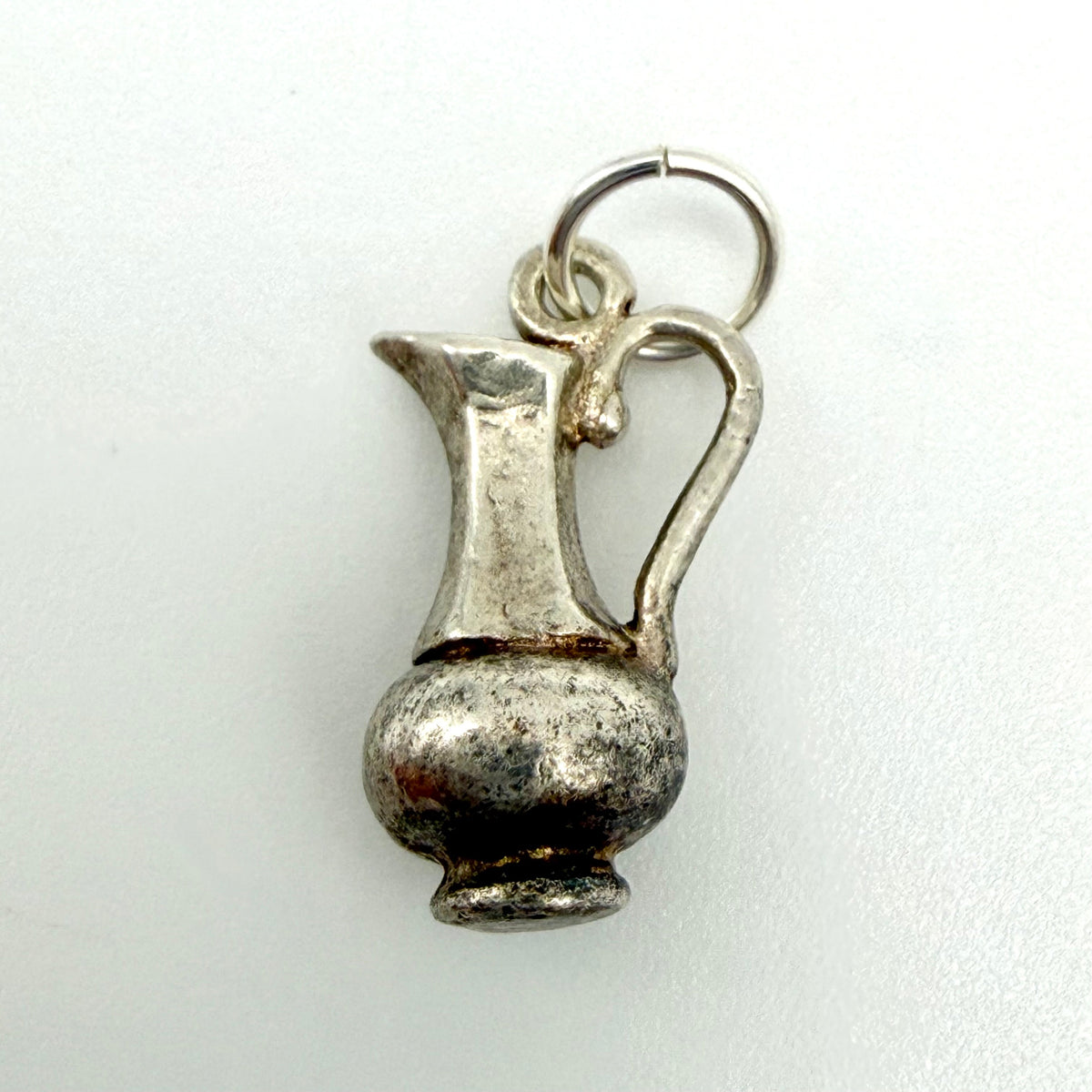 A small silver pitcher charm with a textured, antique finish and a split ring at the top, shown on a plain white background.
