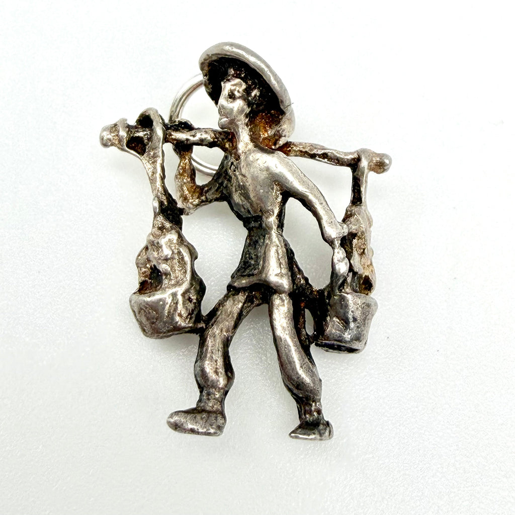 Front of vintage sterling silver water carrier charm beside a ten pence coin