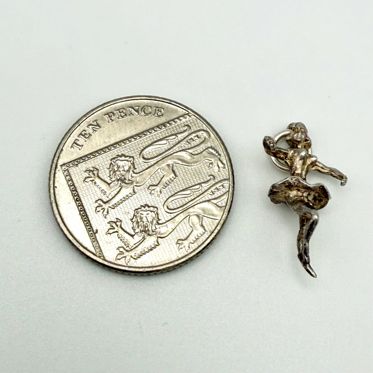 A small silver fairy charm shown next to a silver ten-pence coin for scale, on a plain light gray background.
