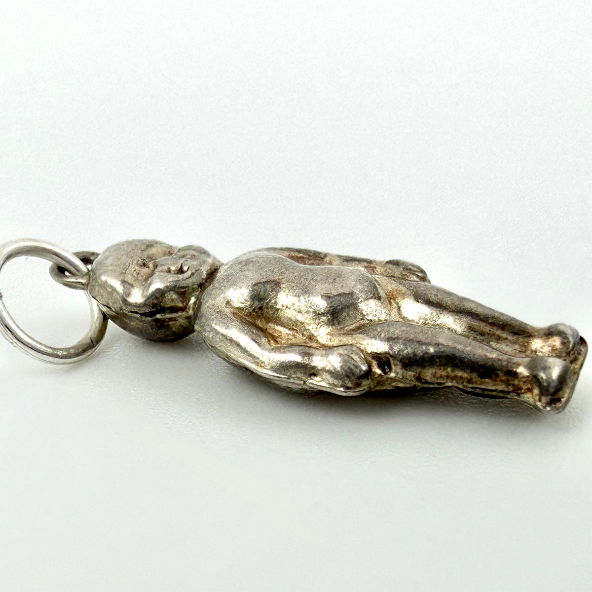 A silver pendant shaped like a reclining figure, attached to a silver ring, photographed on a plain light background.
