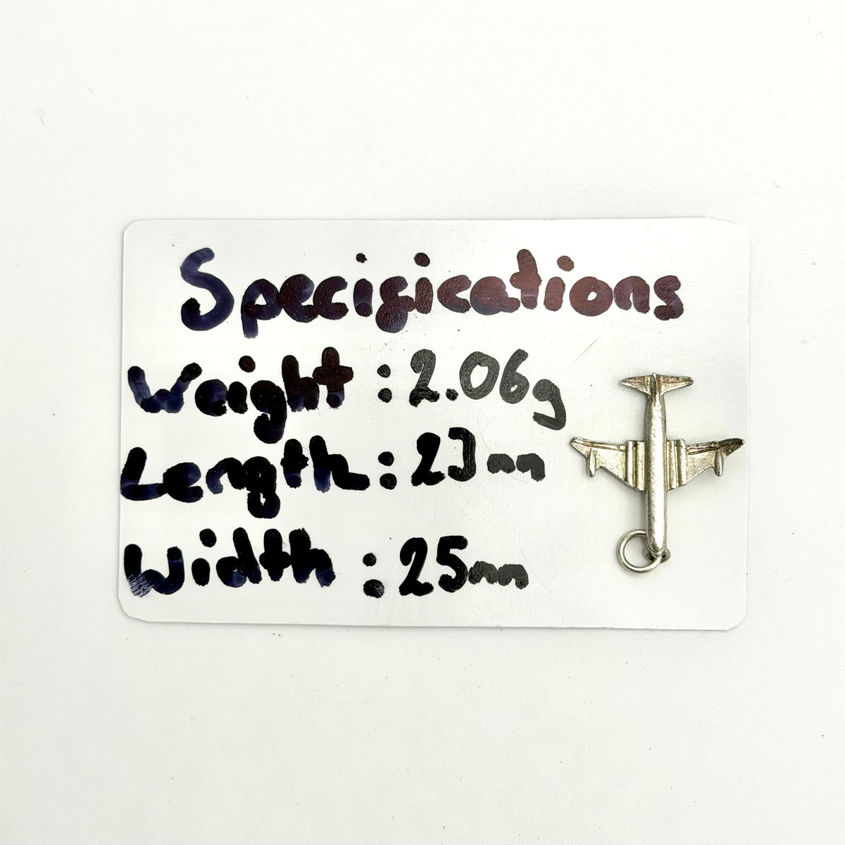 A small silver airplane-shaped pin or charm displayed on a white card with handwritten specifications including weight, length, and width.