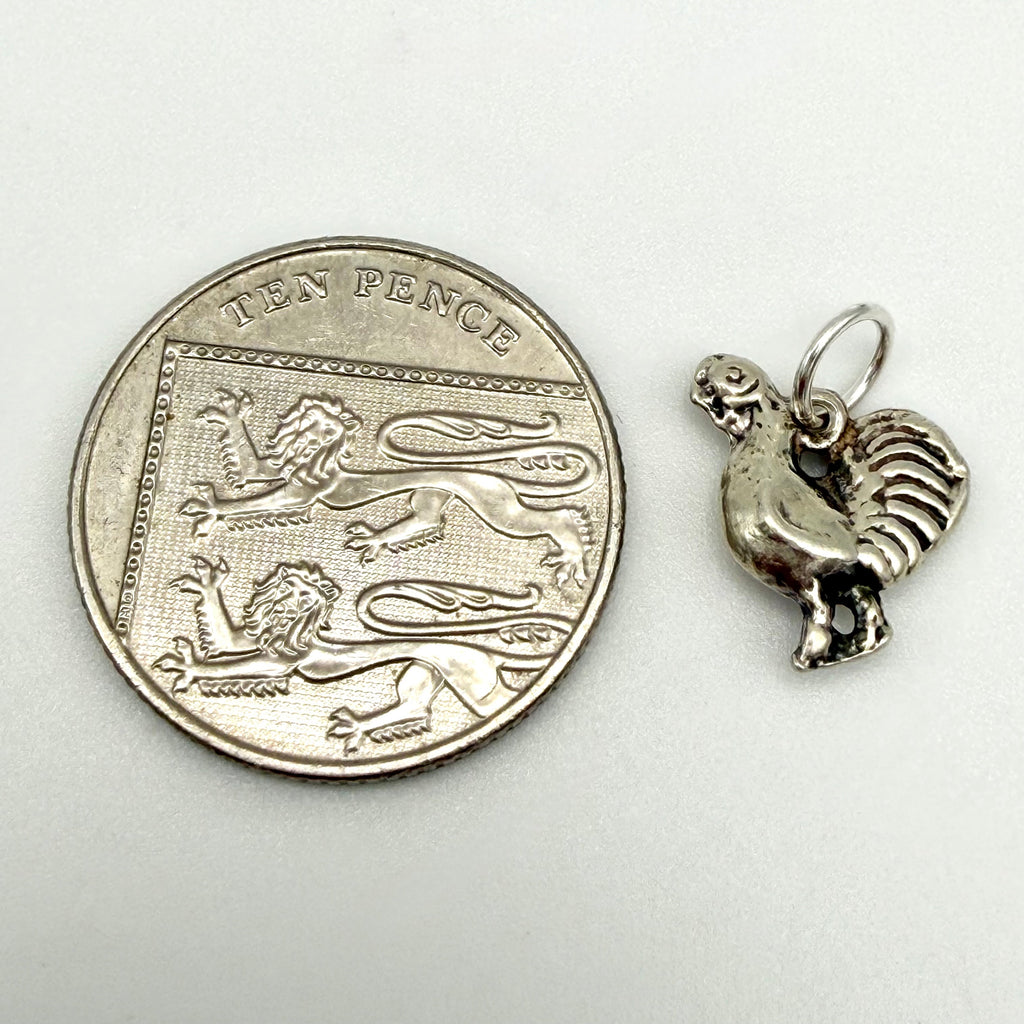 Sterling silver cockerel charm shown beside a ten pence coin for scale