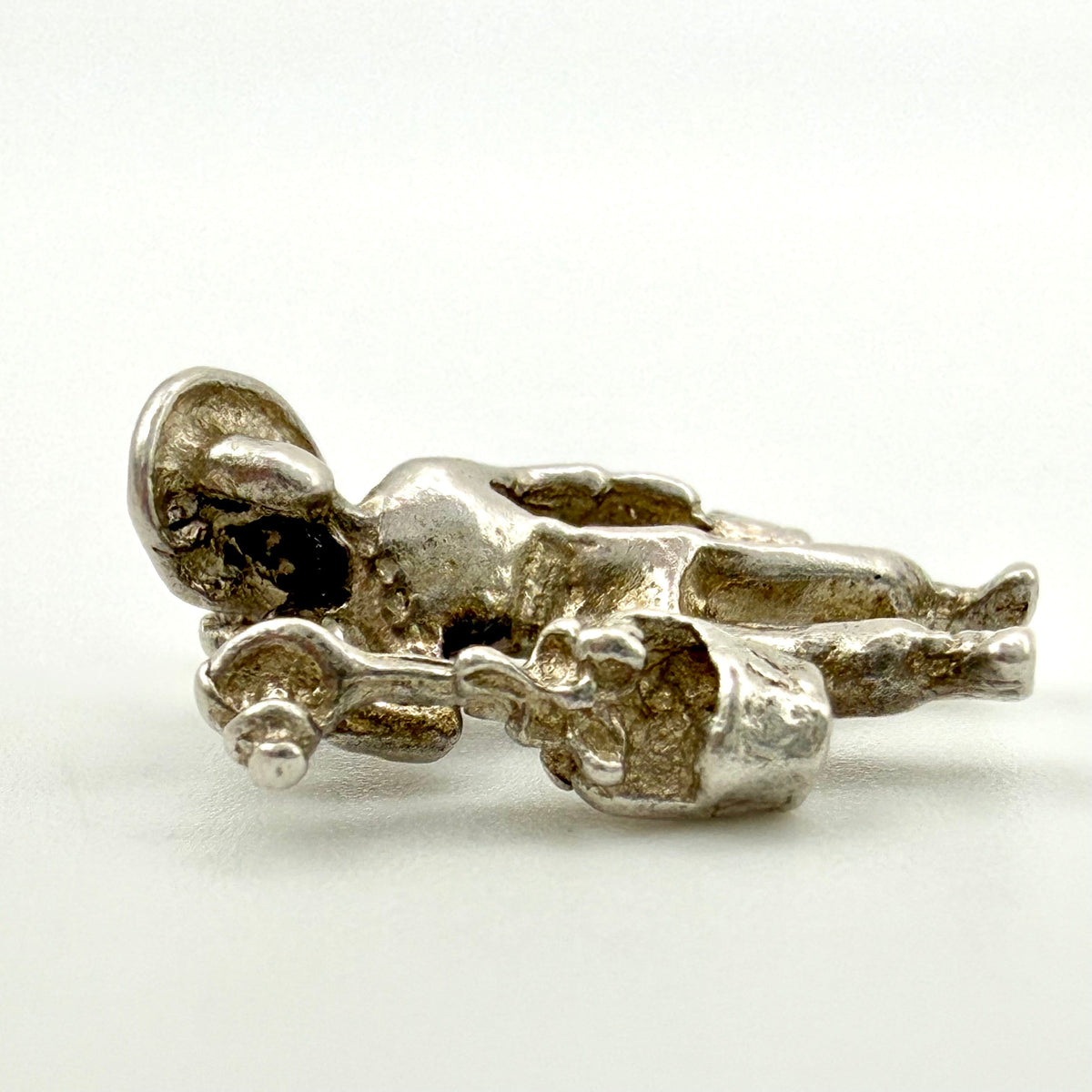A small metallic figurine of a reclining nude human figure holding a shell-like object, photographed on a plain light background.
