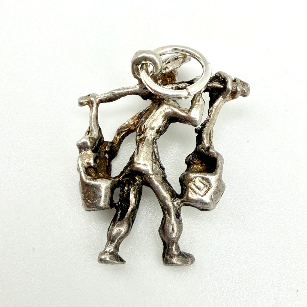 Silver water carrier charm beside handwritten dimensions and weight card
