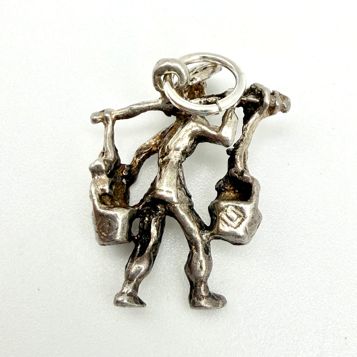 Silver water carrier charm beside handwritten dimensions and weight card