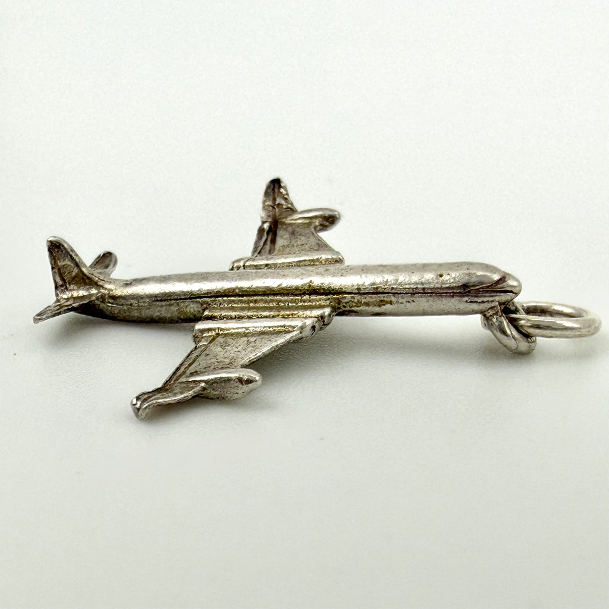A small silver airplane pendant charm with a hanging loop, shown on a plain light background.
