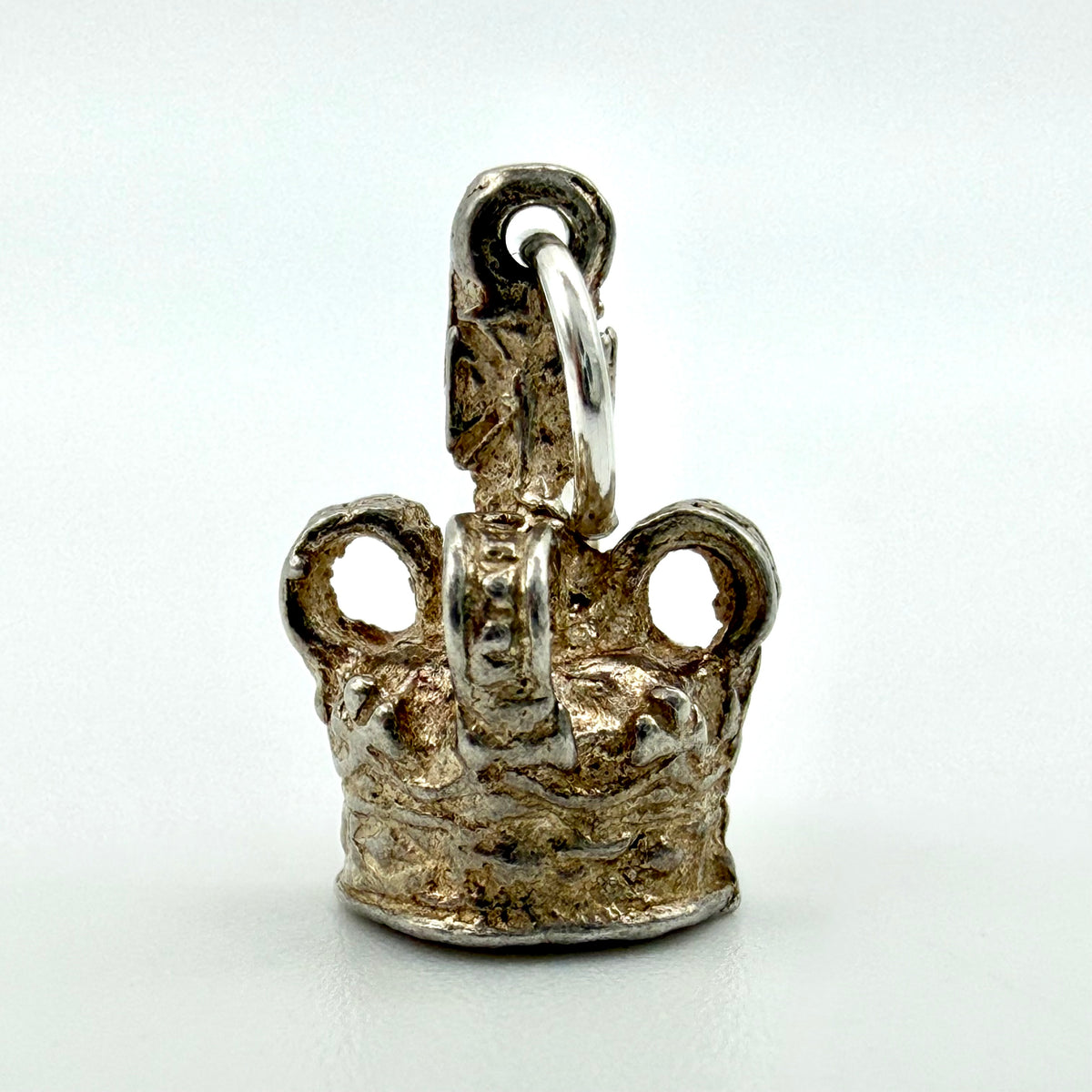 A small sterling silver crown-shaped charm with a textured, hammered finish in silver-toned metal, featuring a loop at the top and a split ring, photographed on a plain light background.