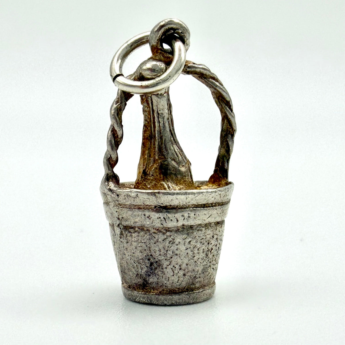 A small sterling silver charm shaped like a rustic wooden bucket with a twisted handle and a hanging loop at the top, shown on a plain light background.