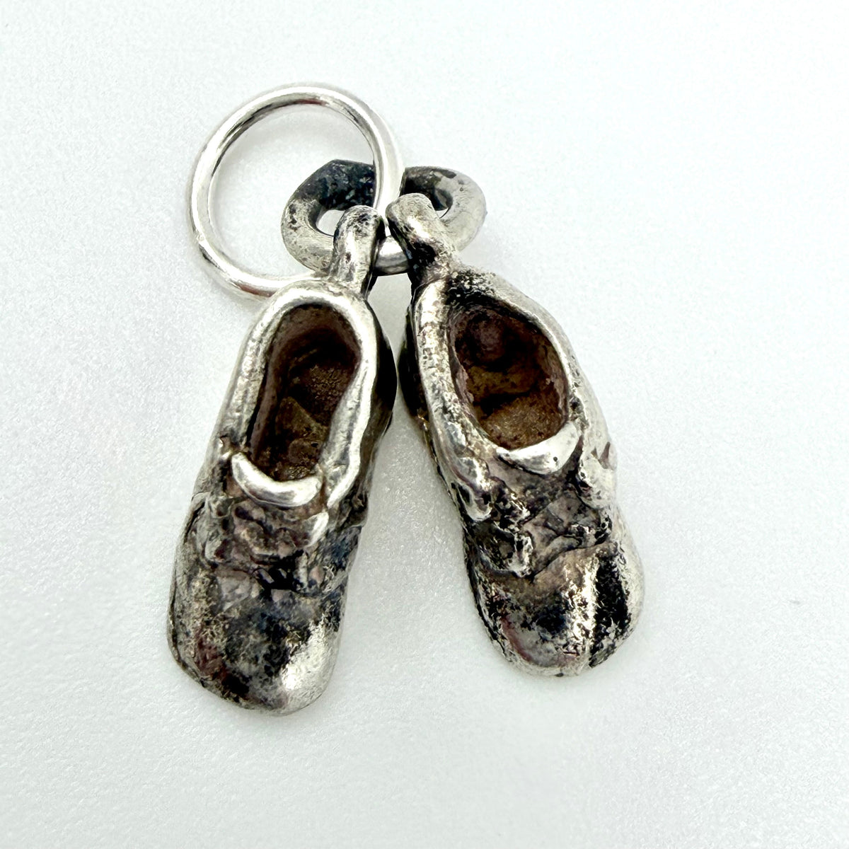 A pair of miniature silver baby booties charms with a silver keyring, displayed on a clean white background.