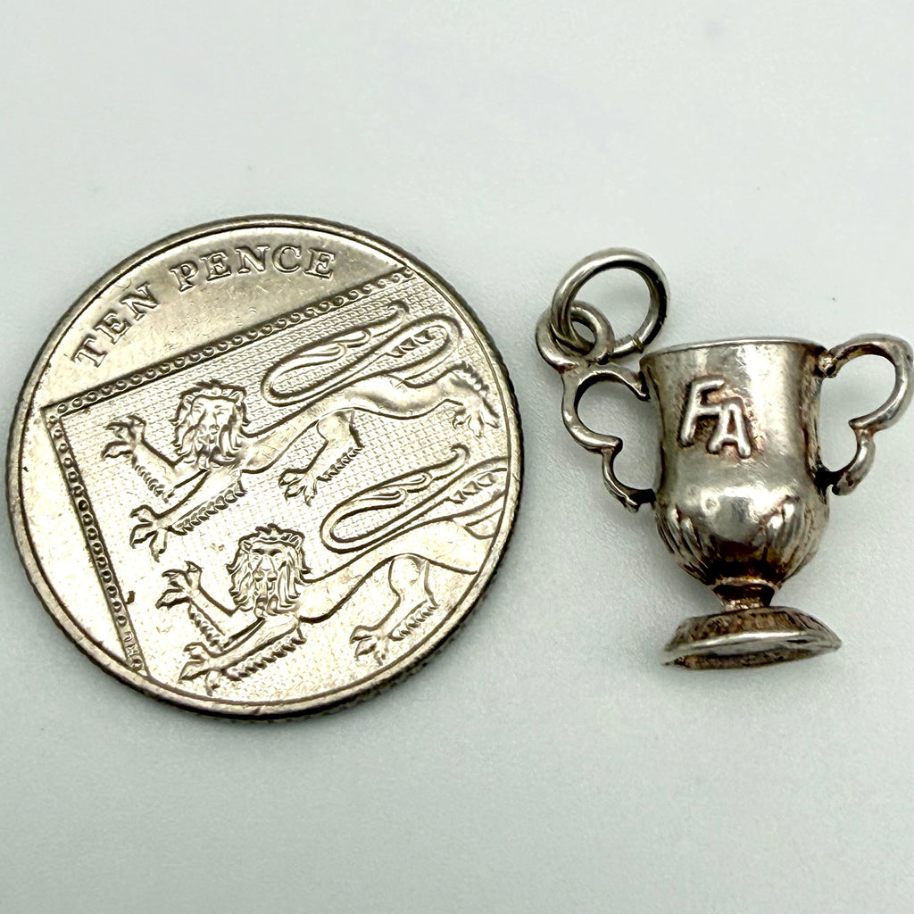 A small silver trophy cup pendant shown next to a UK ten pence coin for scale, on a plain light background.