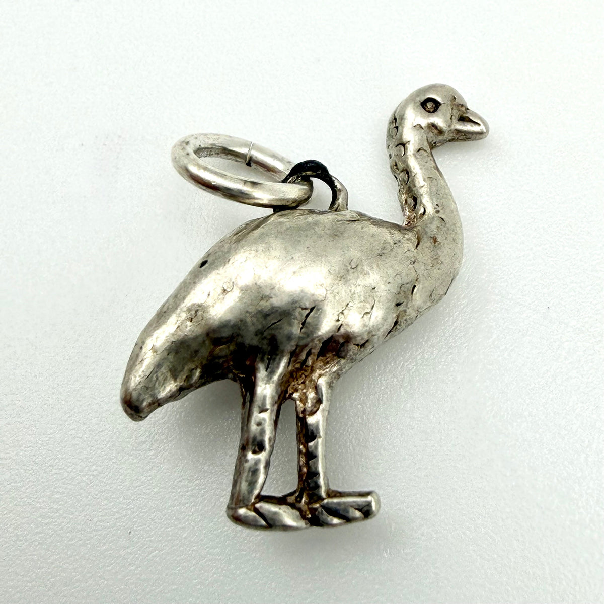 A vintage sterling silver bird charm, shaped like a standing emu or ostrich with a textured patina and a small loop at the top, shown on a plain white background.