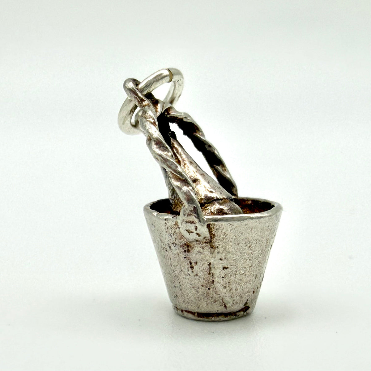 A sterling silver charm shaped like a small metal bucket with twisted rope handles and a hanging loop, shown on a plain light background.
