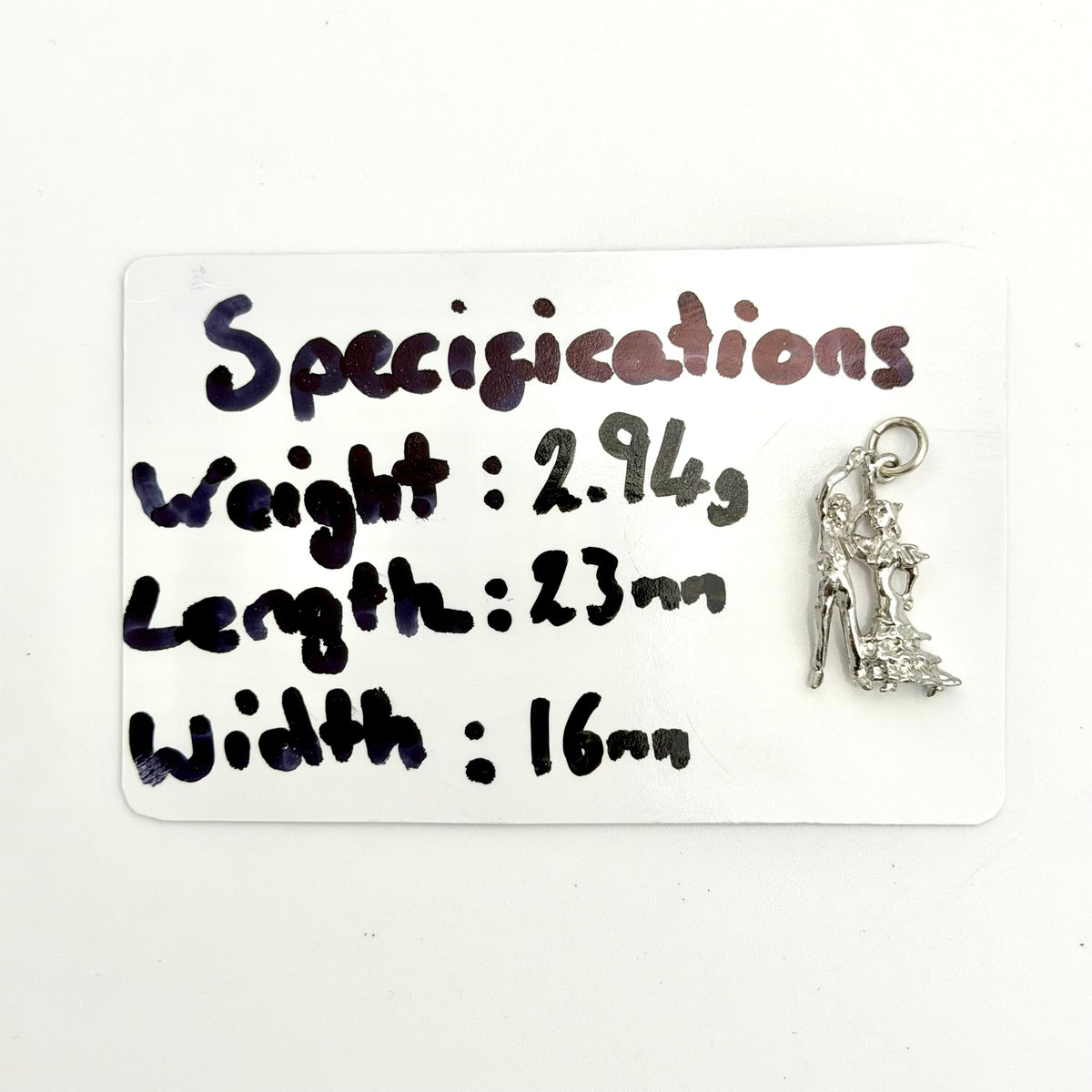 A silver flamenco dancer charm displayed next to a white card with handwritten specifications detailing its weight, length, and width.