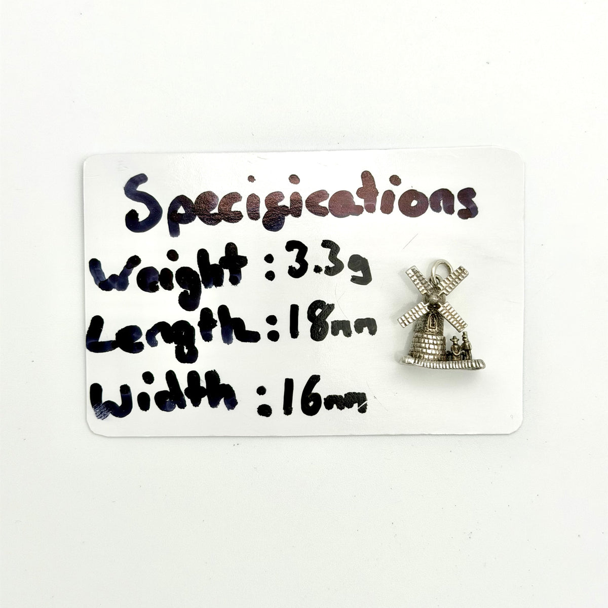 A small silver windmill charm displayed on a white card with handwritten specifications detailing its weight, length, and width.