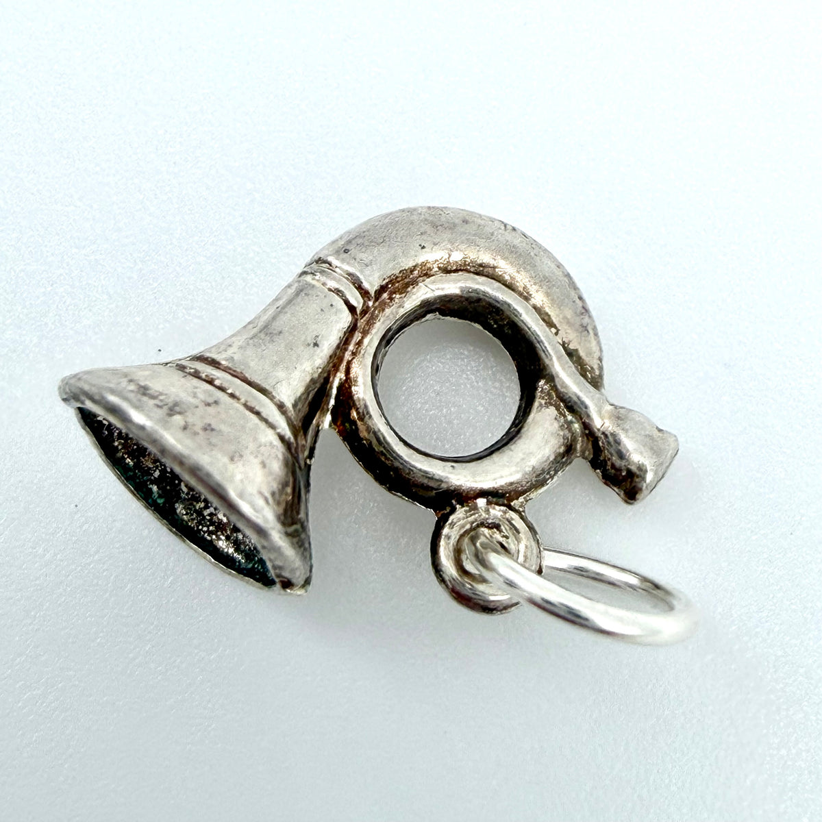 A silver metal horn-shaped charm with a small attached split ring, photographed on a plain light background.