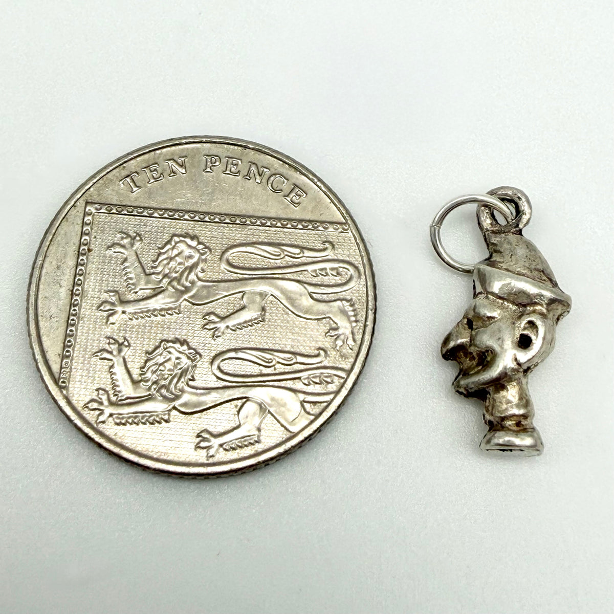 Sterling silver Mr Punch charm beside a ten pence coin for scale